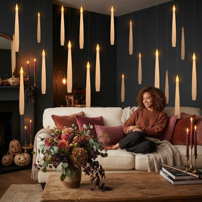 A woman relaxing in a cozy, dark-themed living room decorated with floating LED candles that create a magical atmosphere.
